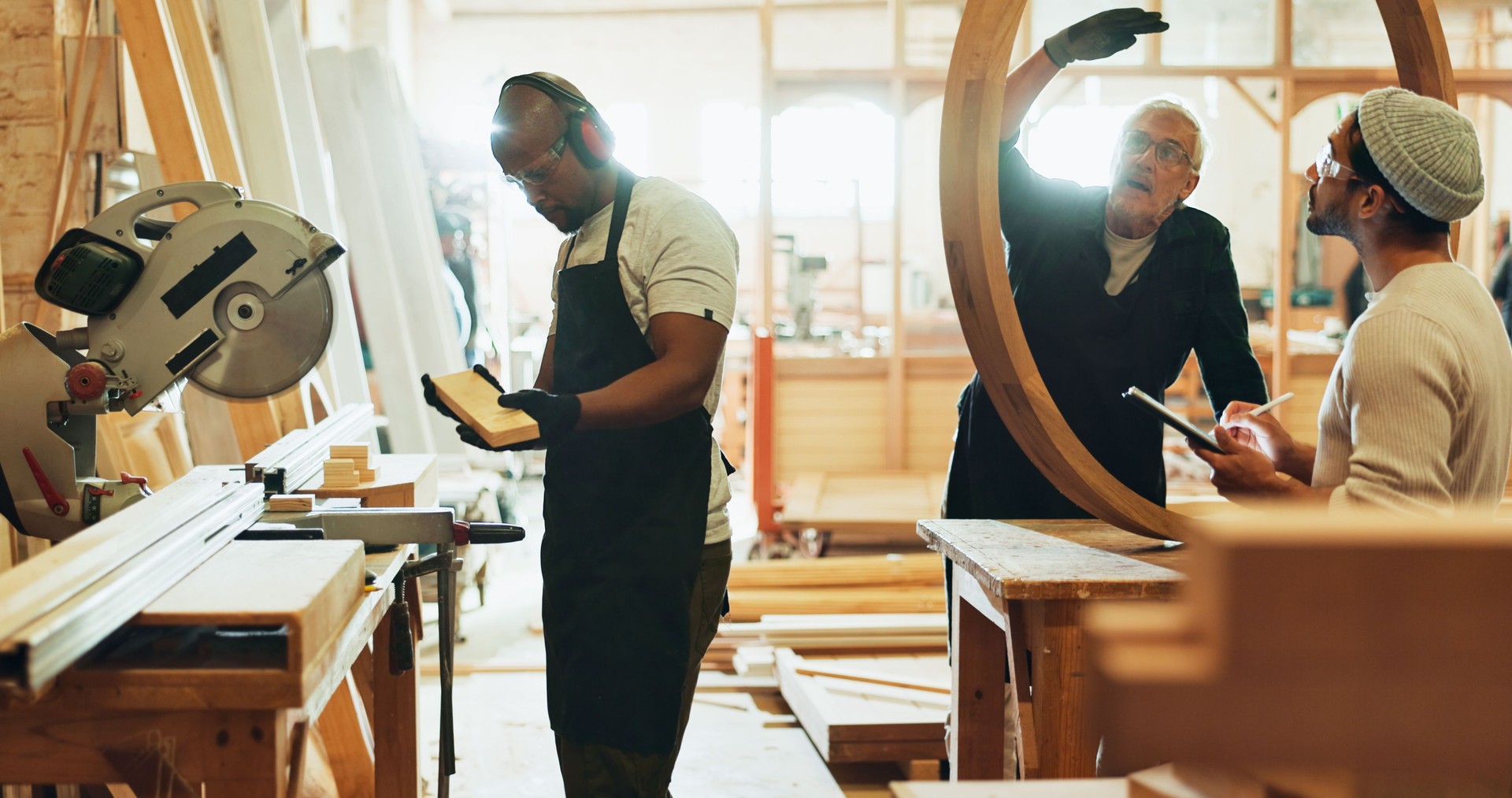 Carpenter, men and teamwork for manufacturing, talking and helping intern with wood work and material. Warehouse, mature mentor and trainee with skills for craftsmanship, people and productivity