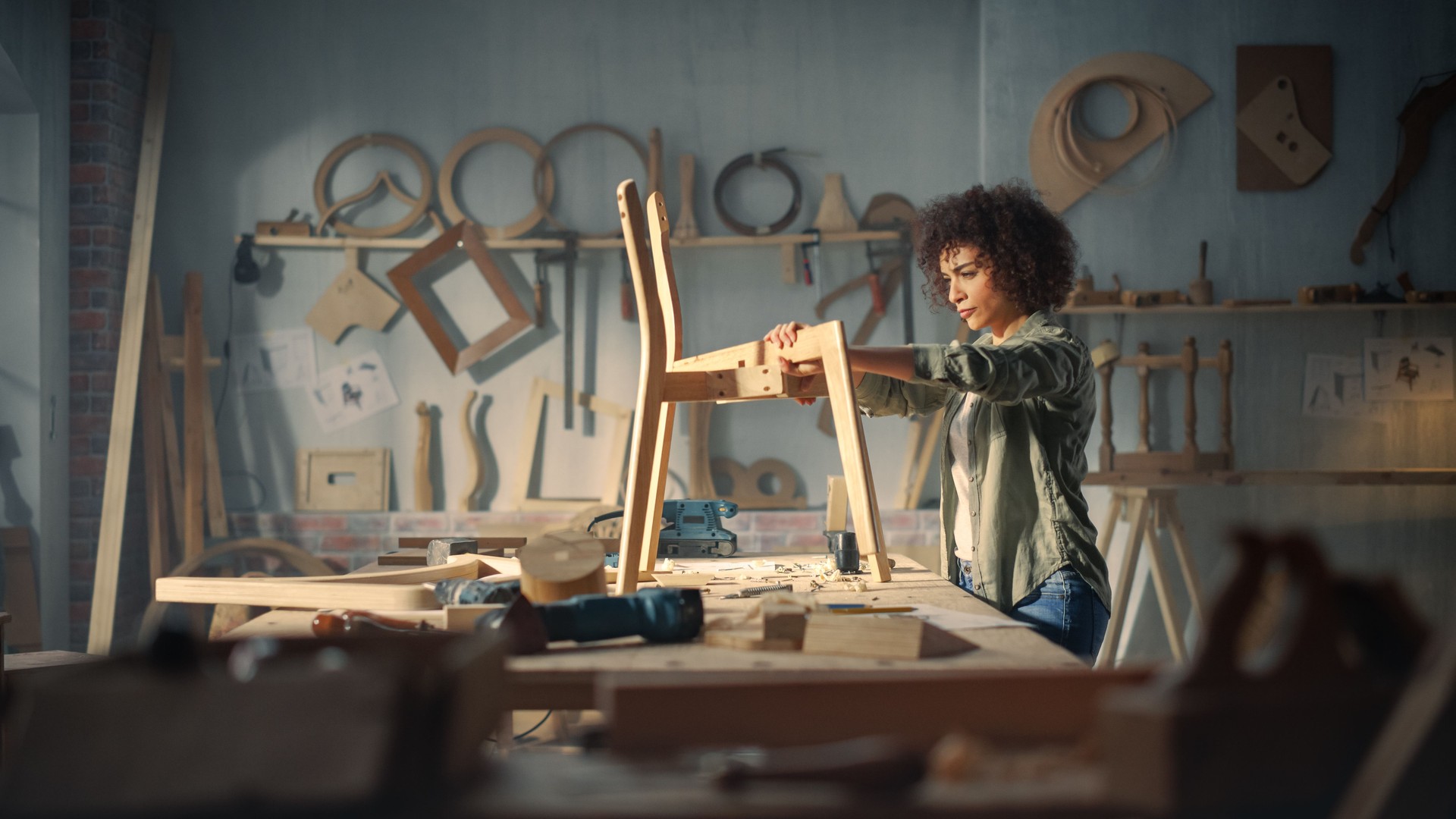 Female Artisan Furniture Designer Marking Out Dimensions on a Blueprint and Starting to Assemble a Wooden Chair. Multiethnic Black Carpenter Working in a Studio